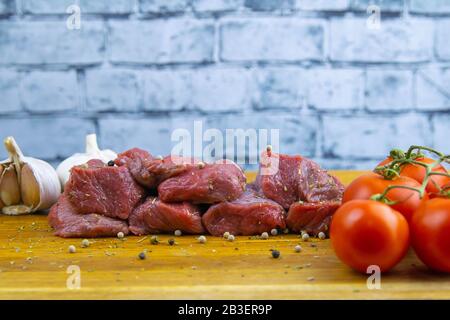 Geschnittene saftige Kalbsscheiben stehen auf einem Holzbrett neben Tomaten und Knoblauch Stockfoto