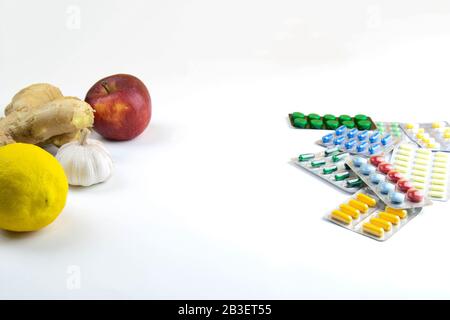 Zitrone, Ingwer, eine Kapelle und Äpfel gegen bunte Tabletten. Das Konzept der Wahl einer gesunden Ernährung im Gegensatz zur Einnahme von Medikamenten Stockfoto
