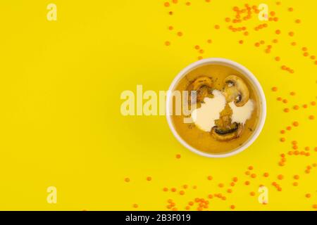 Erbsensuppe mit Pilzen in einem rosafarbenen Teller steht auf gelbem Grund, um die Streuung von Linsensamen Stockfoto