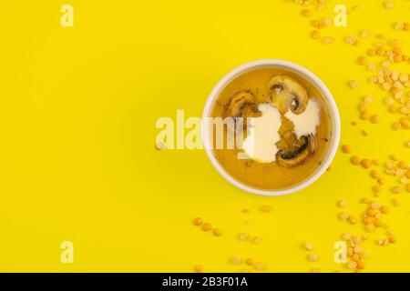 Erbsensuppe mit Pilzen in einem rosafarbenen Teller steht auf gelbem Grund, um die Streuung von Linsensamen Stockfoto