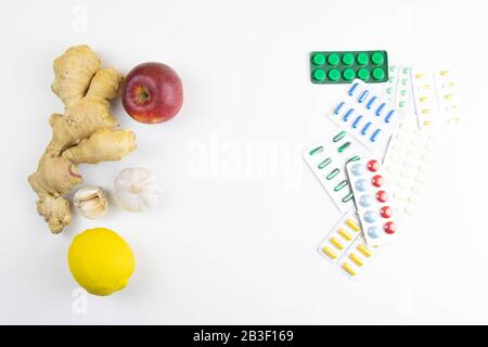 Zitrone, Ingwer, eine Kapelle und Äpfel gegen bunte Tabletten. Das Konzept der Wahl einer gesunden Ernährung im Gegensatz zur Einnahme von Medikamenten Stockfoto