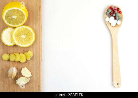 Zitrone, Ingwer und Kapelle gegen mehrfarbige Tabletten. Das Konzept der Wahl einer gesunden Ernährung im Gegensatz zur Einnahme von Medikamenten Stockfoto