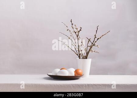 Festliche Ostereier in einer Tonplatte aus Weidenzweigen auf einem Tisch. Lichthintergrund Fröhliches Osterkonzept. Horizontaler Kopierbereich für Rahmen. Stockfoto