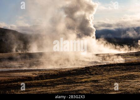 Old Faithful, berühmten Geysir im Yellowstone National Park, Wyoming, USA, explodierende heißen Rauch in der Luft vor dem nächsten Ausbruch mit warmen Sonnenlicht sunr Stockfoto