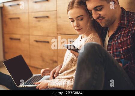 Kaukasische Liebhaber sitzen am Wochenende auf dem Boden und nutzen moderne Technologien Stockfoto
