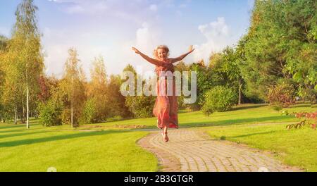 Der Sommer ist die Zeit zum Fliegen. Eine reife Frau in einem fröhlichen Kleid tanzt auf einem Parkhintergrund. Das Alter des Lebens und die Flucht der Seele. Cop Stockfoto