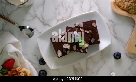 Draufsicht auf Schokoladenbrowsen auf weißem Teller mit Minzblatt oben mit und auf Marmortisch verzierten Blaubeeren Stockfoto