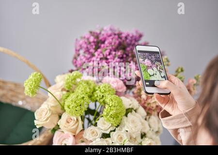 Eine Frau macht ein Foto auf ihrem Telefon mit Blumen. Blumengeschäft Konzept . Blumenfrau schafft Blumenarrangement in einem Korbkorb. . Blumen Lieferung. Stockfoto