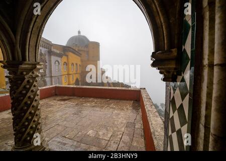 Sintra, Portugal - 18. Januar 2020: Nebliger Tag, der durch die Bögen im Pena Palace zum Rest des Burggeländes peißelt Stockfoto