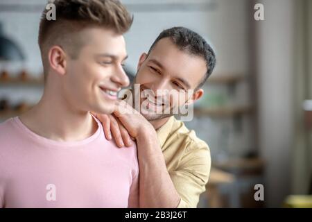 Dunkelhaariger Mann in orangefarbenem Hemd, der die Hände auf die Schulter seiner Partner legt Stockfoto
