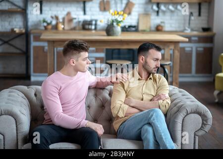 Mann in orangefarbenem Hemd auf dem Sofa sitzend unglücklich und beleidigt aussehend Stockfoto