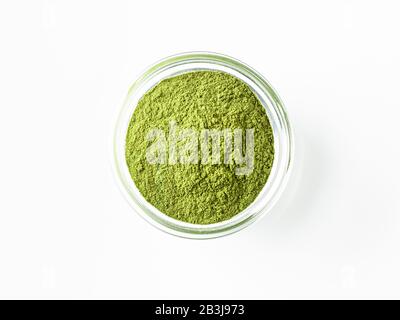 Grünes Matcha-Teepulver in kleiner Glasschale auf weißem Hintergrund. Gepulverter Makcha-Tee, isoliert auf weiß mit Schneideweg. Draufsicht oder flache Lage. Platz für Text oder Design kopieren Stockfoto