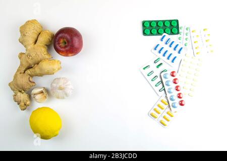 Zitrone, Ingwer, eine Kapelle und Äpfel gegen bunte Tabletten. Das Konzept der Wahl einer gesunden Ernährung im Gegensatz zur Einnahme von Medikamenten Stockfoto