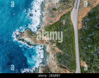 Luftbild der Wellen, die auf dem Felsen neben einer Straße brechen. Hell- und dunkelblauer Wasserschaum, während die Wellen am Ufer brechen. Tiefsee. Big Sur Cali Stockfoto