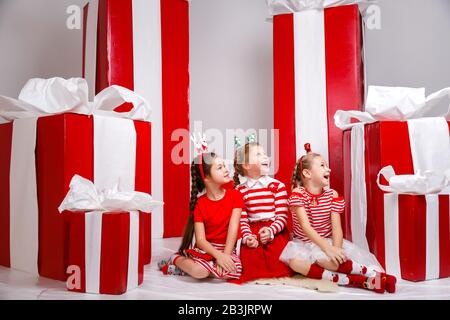 Kleine süße Mädchen im Studio mit Winterferiendekoration und Requisiten. Schöne Mädchen in lustiger Weihnachtskleidung haben Spaß, lebendige Emotionen. Stockfoto