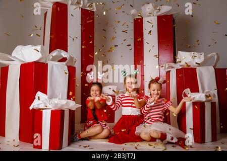 Kleine süße Mädchen im Studio mit Winterferiendekoration und Requisiten. Schöne Mädchen in lustiger Weihnachtskleidung haben Spaß, lebendige Emotionen. Stockfoto