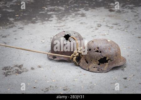 Zwei mit Kugeln perforierte deutsche Militärhelme ziehen auf einem Seil auf Asphalt als Symbol für den Sieg über die Nazi-Eindringlinge. Stockfoto