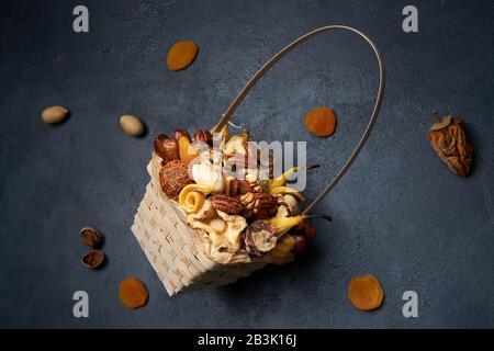 Eckiger Korbkorb mit getrockneten Früchten und Nüssen auf dunkelblauem Grund. Stockfoto