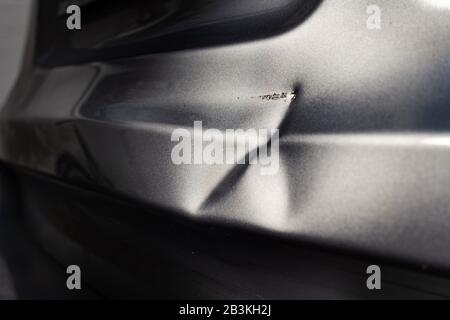 Eine Delle in der Karosserie eines silbernen Autos in aufregendem Licht. Stockfoto