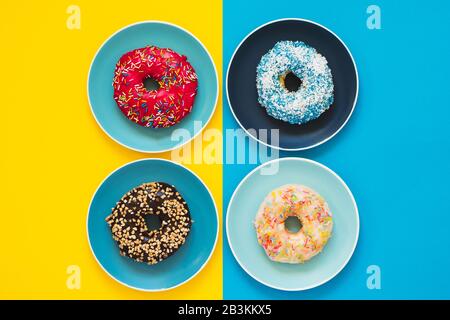 Frische appetitliche 4 Donuts liegen auf dem Teller in gelb-blauem Hintergrund. Konzept der Lieferung von Donuts. Stockfoto