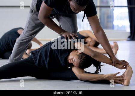 Männliche Tänzerin hilft modernen Tänzern, sich in einem Studio zu Strecken Stockfoto