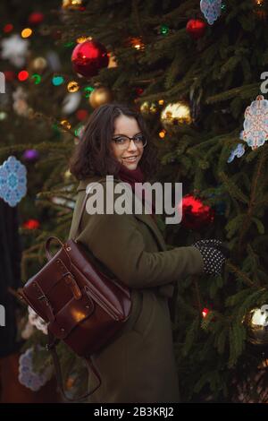 Fröhliches glückliches Mädchen, das auf der Straße schneit. Modische junge Frau mit brünettem Haar, die im Schneefall spazieren geht, Spaß hat und lächelt. Weihnachten m Stockfoto