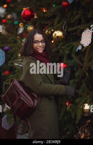 Fröhliches glückliches Mädchen, das auf der Straße schneit. Modische junge Frau mit brünettem Haar, die im Schneefall spazieren geht, Spaß hat und lächelt. Weihnachten m Stockfoto