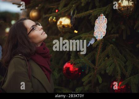 Fröhliches glückliches Mädchen, das auf der Straße schneit. Modische junge Frau mit brünettem Haar, die im Schneefall spazieren geht, Spaß hat und lächelt. Weihnachten m Stockfoto