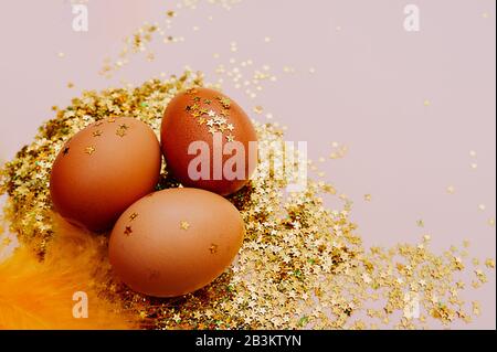 Österliches braunes Ei in einem großen Stapel glänzender Goldsterne auf einem zart rosafarbenen Hintergrund. Fröhlicher Oster-Minimalismus-Mockup, flaches Lay Stockfoto
