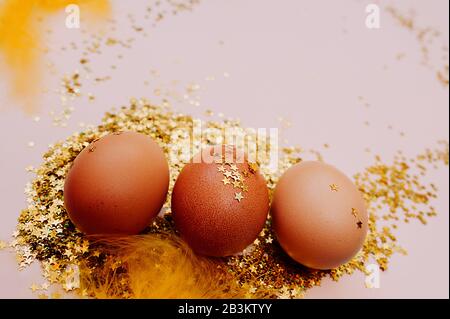 Österliches braunes Ei in einem großen Stapel glänzender Goldsterne auf einem zart rosafarbenen Hintergrund. Fröhlicher Oster-Minimalismus-Mockup, flaches Lay Stockfoto