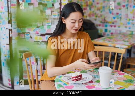 Junge Vietnamesin schaut in einem Café auf Handy Stockfoto