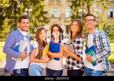 Fröhliche attraktive, diverse fünf Studenten, die in der Nähe der Universität stehen und Notizbücher halten Stockfoto