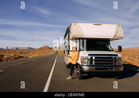 Eine Frau reist mit dem Auto durch das Monument Valley in der Wüste USA und kontrolliert ihr Handy, das auf der Seite der Straße geparkt ist Stockfoto