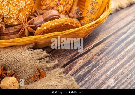 Plätzchen, Schokoladenkuchen, Bagels und Sternanis in einem Korbkorb auf Holzgrund. Nahaufnahme Stockfoto