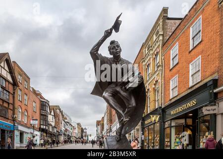 Die Surrey Scholar-Skulptur, die an der Guildford High Street steht. Eine dynamische Skulptur eines Absolventen in Mütze und Gown, die einen Hauch von Büchern überhäuft. Stockfoto