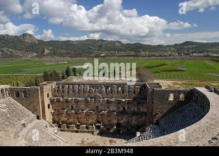 Aspendos ist dafür bekannt, dass es das am besten erhaltene Theater der Antike gibt. Helle grüne Felder im Hintergrund verleihen den antiken Ruinen einen Flair. Stockfoto