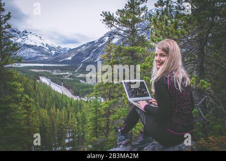 Weibliche digitale Nomade, die remote auf ihrem Laptop in den Bergen der kanadischen rockies arbeitet, qualifizierte Frau Freiberuflerin, die Text auf Laptop tippt Stockfoto