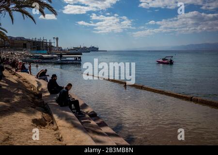 Aqaba, JORDANIEN - 31. JANUAR 2020: Lokale Menschen und Touristen genießen Freitag am sonnigen Stadtstrand mit Glasbodenbooten Urlaub. Winter puffige Wolken Morgenhimmel. Rotseegulf, Haschemitisches Königreich Jordanien Stockfoto