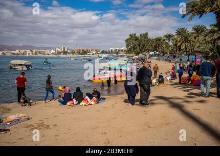 Aqaba, JORDANIEN - 31. JANUAR 2020: Lokale Menschen und Touristen genießen Freitag am sonnigen Stadtstrand mit Glasbodenbooten Urlaub. Winter puffige Wolken Morgenhimmel. Rotseegulf, Haschemitisches Königreich Jordanien Stockfoto