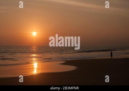 Dies ist ein Sonnenuntergang an der Küste des Ozeans. Die Frau läuft am Meer entlang. Stockfoto