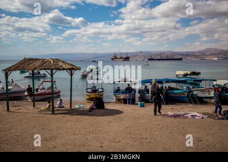 Aqaba, JORDANIEN - 31. JANUAR 2020: Lokale Menschen und Touristen genießen Freitag am sonnigen Stadtstrand mit Glasbodenbooten Urlaub. Winter puffige Wolken Morgenhimmel. Rotseegulf, Haschemitisches Königreich Jordanien Stockfoto