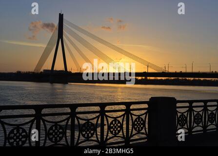 Die Silhouette der Kabelstreusbrücke liegt mit kleinen Wolken gegen den schönen Himmel. Dies ist ein Sonnenuntergang in der europäischen Stadt Riga. Stockfoto