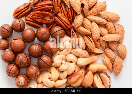 Nahaufnahme mit verschiedenen braunen Nüssen auf grauem Hintergrund. Macadami, Cashews, gehackte Mandeln, Pekannuss gesunde Nahrung Stockfoto