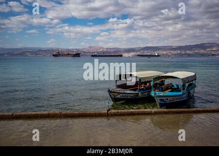 Aqaba, JORDANIEN - 31. JANUAR 2020: Einheimische Männer, Führer mit Glasbodenbooten warten neugierige Touristen, Urlaub Freitag am sonnigen Stadtstrand. Winter puffige Wolken Himmel. Rotseegulf, Königreich Jordanien Stockfoto