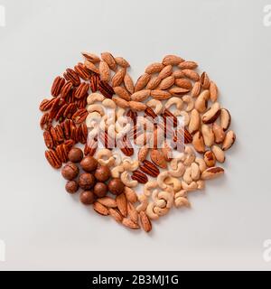 Kreative Komposition aus verschiedenen Walnusspecans, Makadamis, brasilianern, Cashews, Mandeln auf grauem Hintergrund. Mischen Sie die Nüsse in Herzform. Ernährung, balan Stockfoto