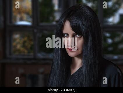 Porträt der gotischen Brunette-Frau, die in einem großen leeren Saal des dunkel düsteren verlassenen Hauses steht Stockfoto