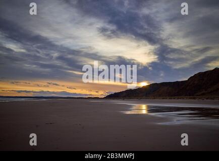 Ein dramatischer Winter-Sonnenuntergang über einem leeren Strand von St. Cyrus an einem kalten Februarabend mit Reflexionen im nassen Sand. Stockfoto