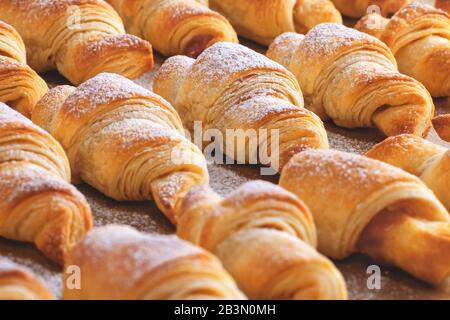 Nahansicht der frisch gebackenen Croissants mit Marmelade, mit Puderzucker auf braunem Backpapier bestreut Stockfoto