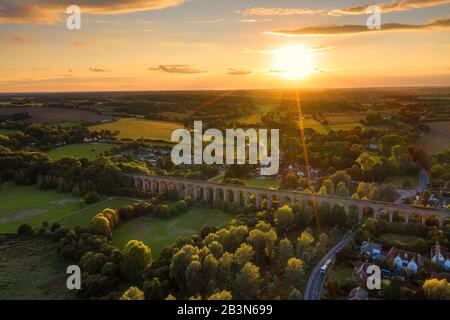 Das Eisenbahnviadukt bei Chappel und weckt Colne in Essex, England, die Sonne eine goldene Kugel direkt über dem Horizont, die Licht und Schatten wirft Stockfoto