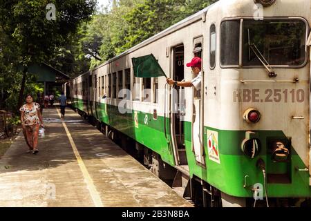 Ein Personenzug am Bahnhof Lanmadaw mit Zugleiter schwenkt eine grüne Flagge und ein Passagier auf dem Bahnsteig, Yangon (Rangun), Myanmar (Birma), Asi Stockfoto